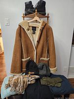 Photo showing the full coat, black boots, scarves, gloves, and knit hats arranged on a chair and floor.