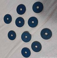 Group of all 10 blue round WWII Canadian meat ration tokens scattered on white cloth background.