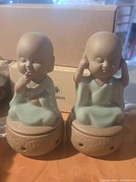 Two baby Buddha incense burners with different hand gestures sitting on beige round bases, ceramic material, new condition.