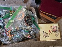 Top-down view of jewelry in plastic bags and paper box with floral design lid, showing mixed jewelry items