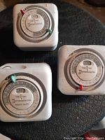 Photo shows three Intermatic plug-in mechanical timers in white plastic cases with circular dials and colored tabs for on/off programming.
