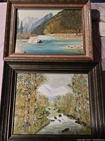 Photo showing two framed landscape paintings, one with mountains and river in a gold-tone frame, one with a forest stream in a dark wood frame.