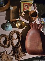 Top view of assorted items showing pineapple-shaped bowl, cigar box, Queen Elizabeth tin, painted gourd, brass bowl, and braided tassels