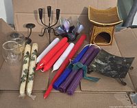 Overview of all candles and candle holders arranged on cardboard surface including wrapped beeswax candles, plain paraffin candles, rolled colored beeswax candles, metal, ceramic, and glass candle holders.