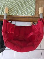 Top view of red padded portable high chair seat showing seat shape and metal support bars with wooden ends.