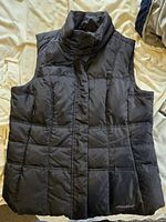 Front view of black Eddie Bauer quilted vest showing high collar and logo embroidery on bottom hem.