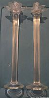Pair of tall, clear glass blown candleholders shown upright on a flat surface with ribbed stems and round bases.