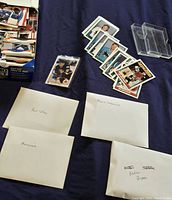Hockey cards spread on a cloth surface with labeled white envelopes for Paul Coffey, Mark Messier, Mario Lemieux and Nolan Ryan, some loose cards and plastic card holders.
