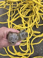 Close-up of the male and female plug ends showing three prongs and molded plastic casing on a heavy duty yellow extension cord.