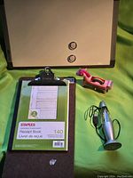 Photo showing whiteboard with two magnets, pink unicorn tape dispenser, USB lava lamp, clipboard with Staples receipt book attached