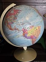 Full front view of the raised relief globe showing North and South America with the metal base and meridian indicator.