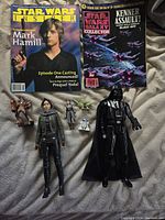 All items laid out on a light grey fabric surface including two Star Wars magazines and six action figures.