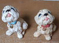 Two puppy figurines, one with a blue collar and one with a red collar, showing front and side angles on a wood surface.