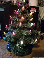 Front view of vintage green ceramic Christmas tree illuminated with multi-color plastic lights.