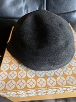 Top view of the black felt hat showing its rounded shape and soft texture, placed on the vintage patterned Eaton's box.
