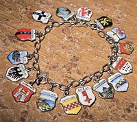 Clear photo of the sterling silver bracelet with all 16 colorful enamel coat of arms pendants laid out flat on a textured surface.