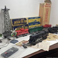 Complete lot showing the vintage American Flyer toy train set including locomotive, cars, tracks, beacon tower, crossing sign, signal tower, original boxes and papers, arranged on a table.