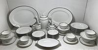 Full set spread, showing dinner plates, platters, bowls, cups and serving pieces with silver trim.