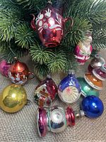 Overview photo of the collection of 11 antique mercury glass Christmas ornaments showing various shapes, colors, and sizes laid on burlap with greenery.