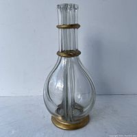 Full view of the clear glass decanter showing bulbous base, long neck, and gold accent rings on base and neck.