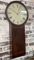 Full front view of clock hanging on brick wall, showing entire case and dial.