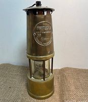 Full view of the brass miners lamp with cylindrical shape and protective glass case around wick.