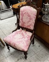 Front angle view of antique Eastlake pink upholstered chair showing the carved walnut frame and fabric condition.