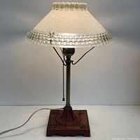 Front view of antique table lamp with illuminated frosted glass shade and cast iron base.