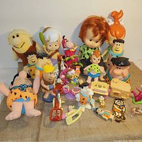 Wide shot of approximately 30 Flintstones themed collectibles including bobbleheads, plush toy, figurines, banks, and playsets.