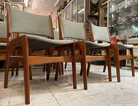 Three-quarter front view showing three chairs with teak frames and light gray-green upholstery