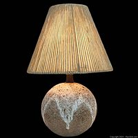 Front view of the lamp lit against black background showing the textured ceramic base and illuminated shade