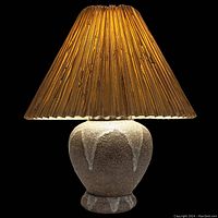 Lamp illuminated in dark background showing lava drip glaze effect and pleated lampshade texture.