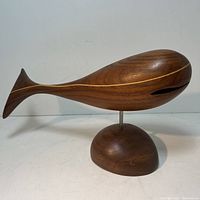 Side view of walnut whale sculpture on stand showing elongated form and wood grain.