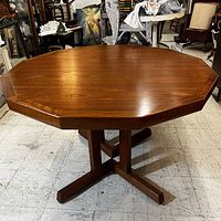 Front angle view of teak dining table showing 12-sided octagonal top and pedestal base with splayed legs.