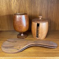 Photo showing wooden goblet, coaster set with case, and pair of wooden salad tongs on a wooden shelf.