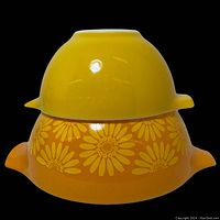 View of both Pyrex bowls stacked, showing yellow daisy patterned larger bowl and solid yellow smaller bowl on top.
