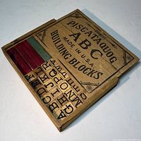 Partially open wooden storage box showing the top portion of colored rectangular blocks inside and printed alphabet on slide-out drawer.