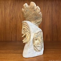 Front and side views of soapstone sculpture showing two False Faces carved in detail and natural beige stone color.