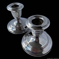 Pair of sterling silver candlesticks with round bases and flared candle holders shown on black background.