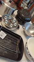 Overview of cookware set on table including spatterware roaster and roasting pan with rack, metal colander, stainless steel steamer/poacher with insert and cups, stockpot with lid, and ceramic mixing bowl.
