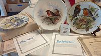 Photo showing two plates with Red Robin and Bluebird illustrations along with certificates of authenticity and display stands.