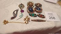 Overview of assortment of costume and Art Deco style jewelry items including pins, clip earrings, brooches, and a chain accessory on a table.