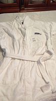 Full front view of white plush terry velour Seahawks robe with waist belt laid flat on table, showing embroidered insignia on pocket