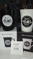 Pair of See's Candy Centennial mugs in black and white, shown on top of their respective original boxes.