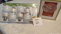 4-pack of white spiral compact fluorescent light bulbs with packaging showing front and backsides on a tablecloth.
