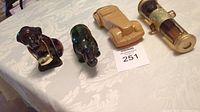 Four vintage Avon collector bottles including St. Bernard dog, rhinoceros, 1937 Cord car, and a cannon, placed on a white patterned tablecloth