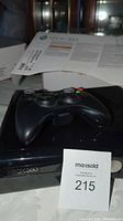 Xbox 360 console with controller and MaxSold lot badge on table, original paper manual partially visible.