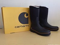 Pair of black Carhartt boots standing upright next to a yellow Carhartt box with logo.