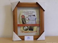 Collectors Cabinet wooden frame display case with package label inside showing items to display.