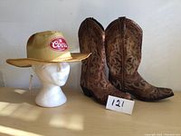 Full view of the cowboy boots and straw hat on a surface showing overall appearance and details of the items.